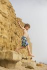 Junge in Badehose springt auf Strandfelsen — Stockfoto