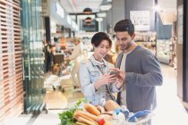 Young couple using cell phone in grocery store market — Stock Photo