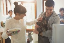 Young couple petting cat in kitchen — Stock Photo