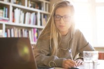 Chica adolescente con auriculares haciendo la tarea con el ordenador portátil - foto de stock