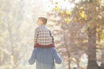 Vater trägt Sohn auf Schultern unter Herbstlaub — Stockfoto