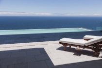 Cadeiras de estar e piscina infinita com vista para o mar — Fotografia de Stock