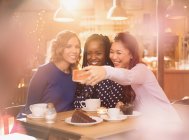 Sonriendo a las mujeres amigas tomando selfie con el teléfono de la cámara en la mesa de café - foto de stock