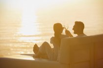 Silhouette couple toasting verres à vin sur chaise longue avec vue sur l'océan coucher de soleil — Photo de stock