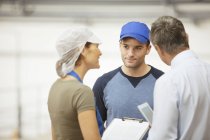 Supervisor y trabajadores hablando en planta de procesamiento de alimentos - foto de stock