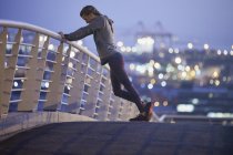 Жіночий бігун розтягує ноги на міському пішохідному мосту на світанку — стокове фото