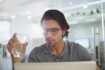 Geschäftsmann mit Kopfhörern trinkt Wasser am Laptop — Stockfoto