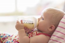 Baby girl drinking from bottle on sofa — Stock Photo