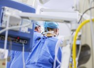 Visão traseira dos médicos em sala de operações, equipamentos médicos em primeiro plano — Fotografia de Stock