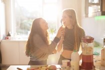 Teenage girls playing with spoon in sunny kitchen — Stock Photo