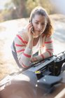 Frustrierte Frau telefoniert mit Handy und schaut auf Auto-Motor — Stockfoto