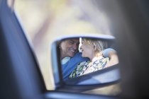 Side-view mirror reflection of couple hugging inside car — Stock Photo