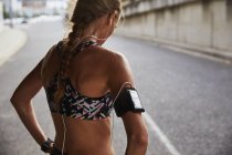 Ajuste corredor femenino en sujetador deportivo con brazalete reproductor de mp3 y auriculares descansando en la calle urbana - foto de stock