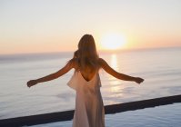 Жінка з простягнутими руками дивиться спокійний вид на захід сонця над океанським горизонтом — стокове фото