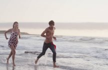 Молода пара біжить в океанічному серфінгу — стокове фото