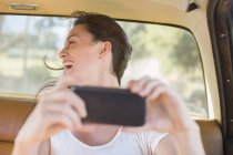 Mulher no banco de trás do carro tirando foto com telefone celular — Fotografia de Stock