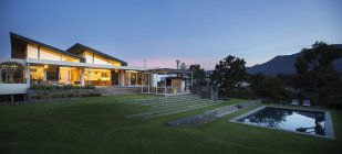 Illuminated modern house beyond yard and swimming pool at night — Stock Photo