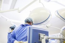Вид сзади на врача в хирургической шапке, маске и халате в операционной — стоковое фото