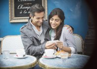 Пара, пользующаяся телефоном в кафе на тротуаре, Париж, Франция — стоковое фото