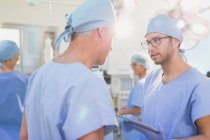 Чоловічі хірурги з цифровим планшетом розмовляють в операційній кімнаті — стокове фото