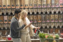 Young couple using cell phone, grocery shopping in market — Stock Photo