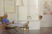 Mann mit digitalem Tablet entspannt sich, spricht mit Frau in Badewanne im Luxus-Hotelzimmer — Stockfoto