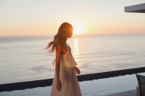 Mulher de vestido branco no tranquilo pátio de luxo com vista para o mar ao pôr do sol — Fotografia de Stock