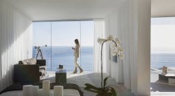 Mulher de pé na moderna casa de luxo vitrine varanda com vista para o mar ensolarada — Fotografia de Stock