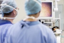 Visão traseira de dois cirurgiões olhando para o monitor durante a cirurgia em sala de cirurgia — Fotografia de Stock