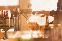 Cropped image of bartender pouring beer from beer tap behind bar — Stock Photo