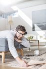 Man with headphones reading newspaper and drinking coffee in living room — Stock Photo
