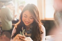 Sorrindo chinês mulher mensagens de texto com telefone celular no café — Fotografia de Stock