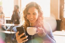 Frau mit Ohrhörern trinkt Cappuccino und Video-Chat im Café — Stockfoto