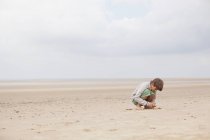 Menino brincando na areia na praia nublada de verão — Fotografia de Stock