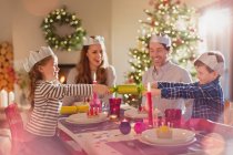 Família em coroas de papel puxando cracker de Natal na mesa de jantar — Fotografia de Stock