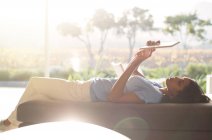 Femme posée sur chaise longue en utilisant une tablette numérique sur terrasse ensoleillée — Photo de stock