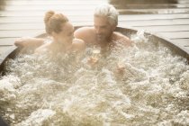 Casal sorridente bebendo champanhe na banheira de hidromassagem no pátio — Fotografia de Stock