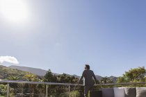 Empresário em pé no pátio varanda abaixo do céu azul ensolarado — Fotografia de Stock