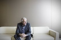Homme âgé sur le canapé regardant loin au bureau moderne — Photo de stock
