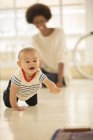Mother watching baby boy crawl on floor at home — Stock Photo
