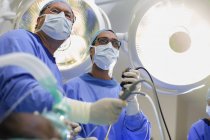 Visão de baixo ângulo de dois cirurgiões segurando equipamentos de laparoscopia em sala de operações — Fotografia de Stock