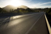 Sun shining over mountains and open road — Stock Photo