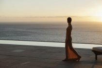 Femme regardant l'océan depuis le patio moderne au coucher du soleil — Photo de stock