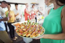 Woman serving tray of food at party — Stock Photo