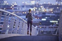 Female runner running on urban footbridge at dawn — Stock Photo
