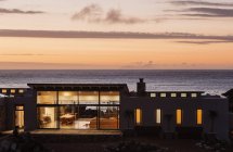 Illuminated luxury home overlooking ocean at sunset — Stock Photo