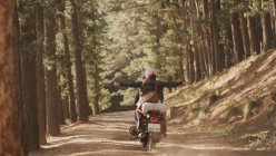 Ausgelassene junge Frau fährt Motorrad auf Feldweg im Wald — Stockfoto