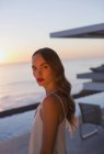 Portrait serious, beautiful woman on sunset patio with ocean view — Stock Photo