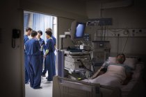 Paziente sdraiato a letto in unità di terapia intensiva, team di medici che discutono in background — Foto stock