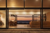 Illuminated home showcase interior overlooking ocean at sunset — Stock Photo